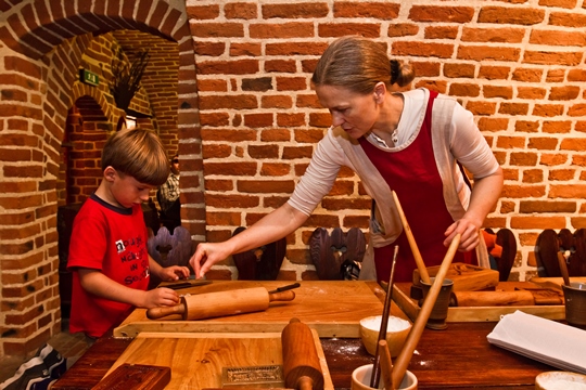interior de una casa antigua de ladrillo donde una mujer le enseña a un niño cómo preparar los pasteles de miel